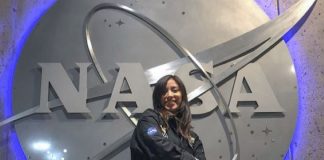 A young woman wearing a NASA jumper poses in front of a massive NASA logo