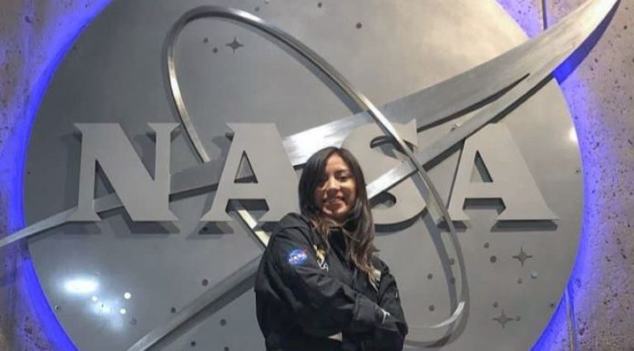 A young woman wearing a NASA jumper poses in front of a massive NASA logo