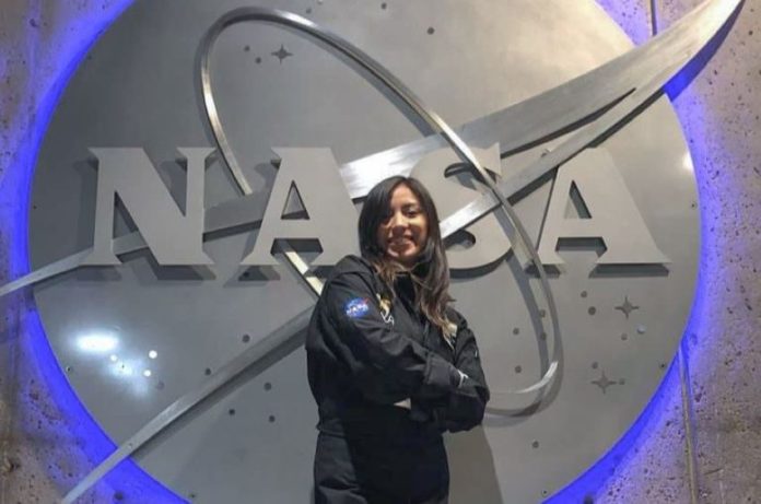 A young woman wearing a NASA jumper poses in front of a massive NASA logo