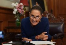 Mexican President Claudia Sheinbaum leans over her desk and smiles