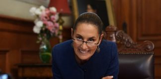 Mexican President Claudia Sheinbaum leans over her desk and smiles