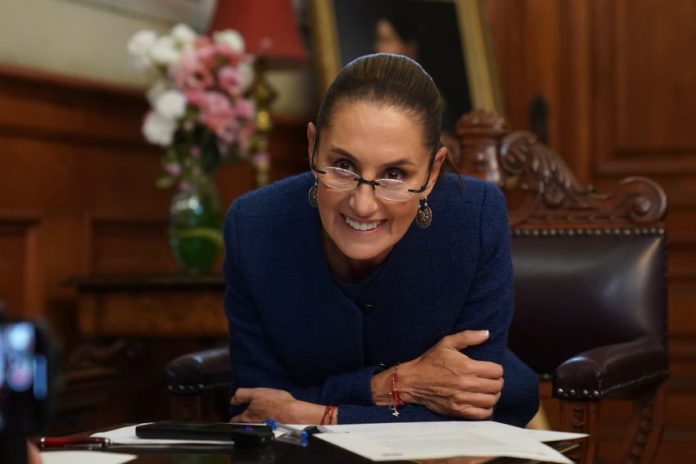 Mexican President Claudia Sheinbaum leans over her desk and smiles