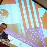 Mexico's Economy Minister Marcelo Ebrard sitting at a panel discussion table onstage with his name placard in front of him and a jug of water. Behind him is a projection screen with images of the Mexican, Canadian and US flags and Spanish words saying "International Seminar: North America: What lies ahead"