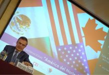 Mexico's Economy Minister Marcelo Ebrard sitting at a panel discussion table onstage with his name placard in front of him and a jug of water. Behind him is a projection screen with images of the Mexican, Canadian and US flags and Spanish words saying "International Seminar: North America: What lies ahead"