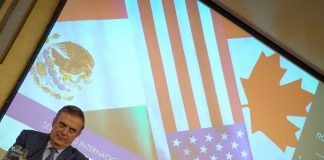 Mexico's Economy Minister Marcelo Ebrard sitting at a panel discussion table onstage with his name placard in front of him and a jug of water. Behind him is a projection screen with images of the Mexican, Canadian and US flags and Spanish words saying "International Seminar: North America: What lies ahead"