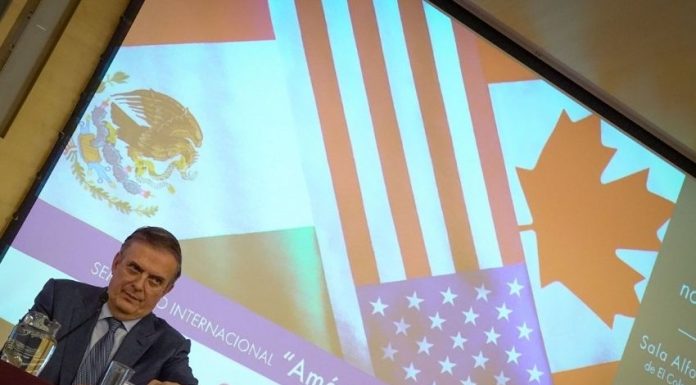 Mexico's Economy Minister Marcelo Ebrard sitting at a panel discussion table onstage with his name placard in front of him and a jug of water. Behind him is a projection screen with images of the Mexican, Canadian and US flags and Spanish words saying "International Seminar: North America: What lies ahead"