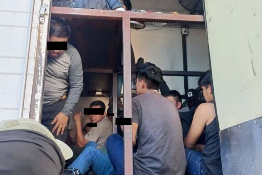 male migrants ranging from youths to middle-aged inside a tractor trailer truck whose inside is built with a metal framework to allow people to be stacked on "shelves" on top of each other.