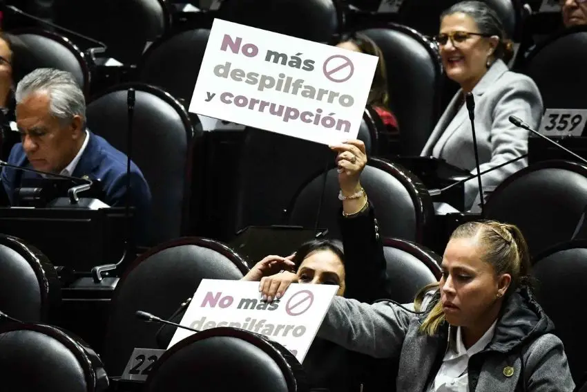 Morena lawmakers in Mexico's Chamber of Deputies in their seats, a few holding signs saying in Spanish "no mas despilfarro y corrupcion."