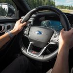 Hands grip the wheel of a Ford car as it drives down a highway