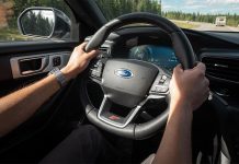 Hands grip the wheel of a Ford car as it drives down a highway