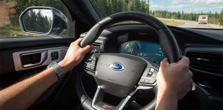 Hands grip the wheel of a Ford car as it drives down a highway