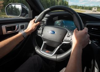 Hands grip the wheel of a Ford car as it drives down a highway