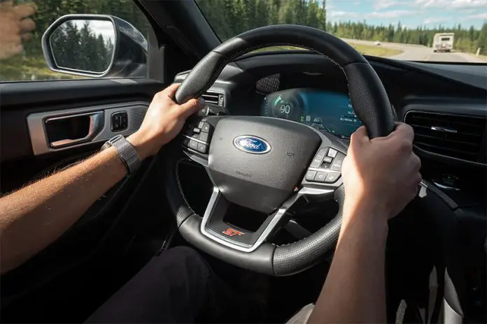 Hands grip the wheel of a Ford car as it drives down a highway