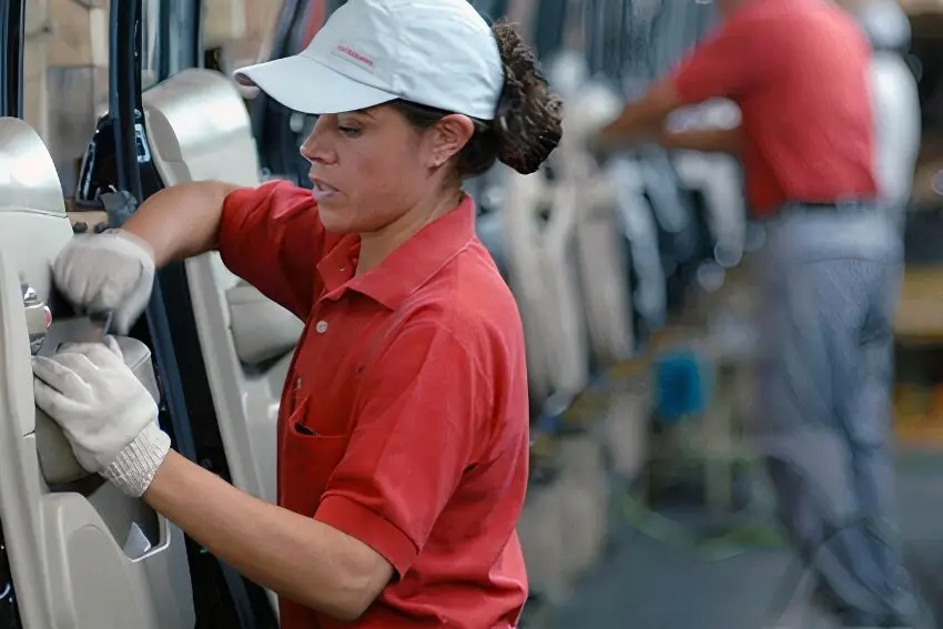 Mexican woman working on a Mexican factory assembly line wearing a cap and a red uniform polo shirt.