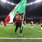 A football player runs with a Mexican flag across the field of Mexico City's Aztec Stadium