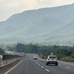 An SUV drives down a highway in Mexico towards distant green mountains