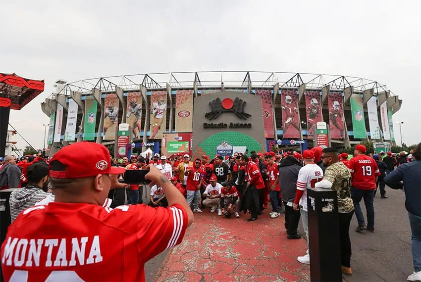 People in red jerseys take photos outside a stadium bearing the words "Estadio Azteca"