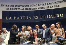 Senate President Gerardo Fernández Noroña, of the Morena party, sits on a legislative dias in front of the words "La Patria Es Primera" as lawmakers argue behind him.