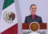 Mexican President Claudia Sheinbaum stands at a podium during her morning press conference in front of a Mexican flag