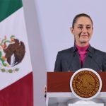 Mexican President Claudia Sheinbaum stands at a podium during her morning press conference in front of a Mexican flag