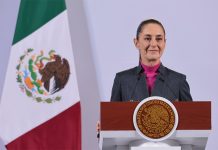 Mexican President Claudia Sheinbaum stands at a podium during her morning press conference in front of a Mexican flag