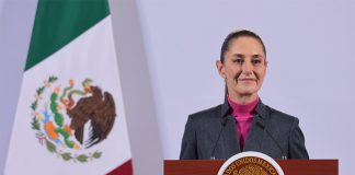 Mexican President Claudia Sheinbaum stands at a podium during her morning press conference in front of a Mexican flag