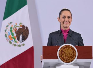 Mexican President Claudia Sheinbaum stands at a podium during her morning press conference in front of a Mexican flag