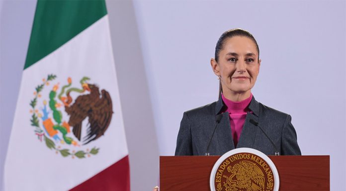 Mexican President Claudia Sheinbaum stands at a podium during her morning press conference in front of a Mexican flag