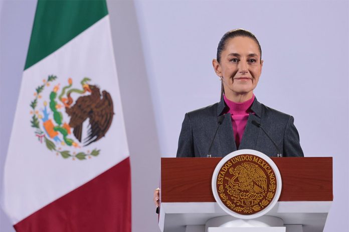 Mexican President Claudia Sheinbaum stands at a podium during her morning press conference in front of a Mexican flag