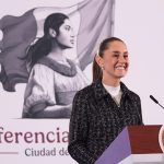 Mexico's President Claudia Sheinbaum stands at a podium smiling during her morning press conference.