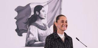 Mexico's President Claudia Sheinbaum stands at a podium smiling during her morning press conference.
