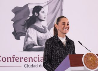 Mexico's President Claudia Sheinbaum stands at a podium smiling during her morning press conference.