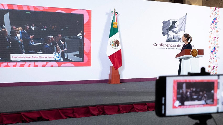 President Sheinbaum turns from her podium to look at a screen showing a Mexican Senate session, during her Friday mañanera or press conference