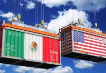 Illustration of two shipping containers hanging by cables in the air. The front of the container on stage left is painted with he flag of Mexico. The container on stage right is painted with the flag of the United States.