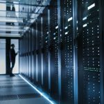 The silouette of a person is visible at the end of a data center hallway filled with computer servers