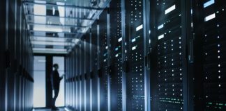 The silouette of a person is visible at the end of a data center hallway filled with computer servers