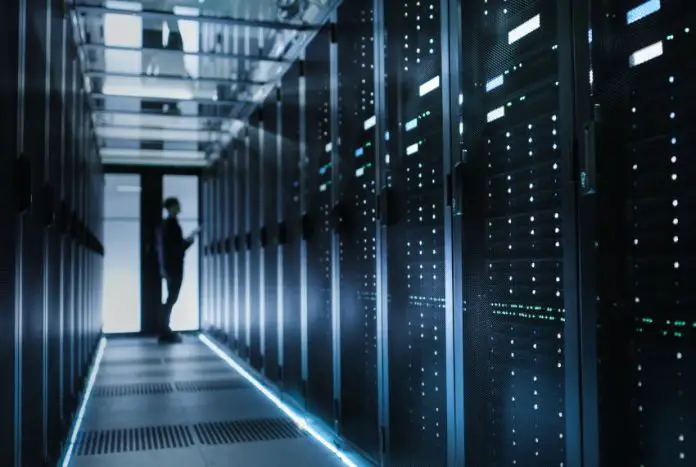 The silouette of a person is visible at the end of a data center hallway filled with computer servers