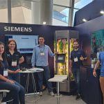 Young Siemens Mexico employees smile and pose for a photo with a tank full of experimentally grown lettuce