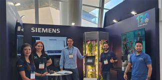 Young Siemens Mexico employees smile and pose for a photo with a tank full of experimentally grown lettuce