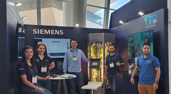 Young Siemens Mexico employees smile and pose for a photo with a tank full of experimentally grown lettuce