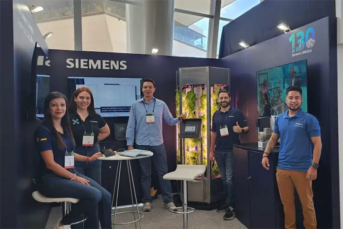 Young Siemens Mexico employees smile and pose for a photo with a tank full of experimentally grown lettuce