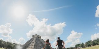 A couple runs through the Chichén Itzá archaeological site on a sunny day.