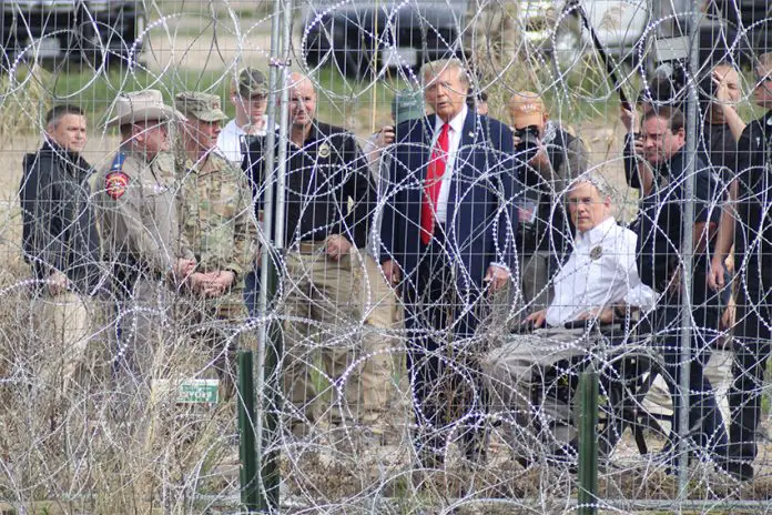 Presidential candidate Donald Trump looks through border fencing in El Paso, Texas, during a campaign stop, surrounded by Texas rangers and border patrol agents