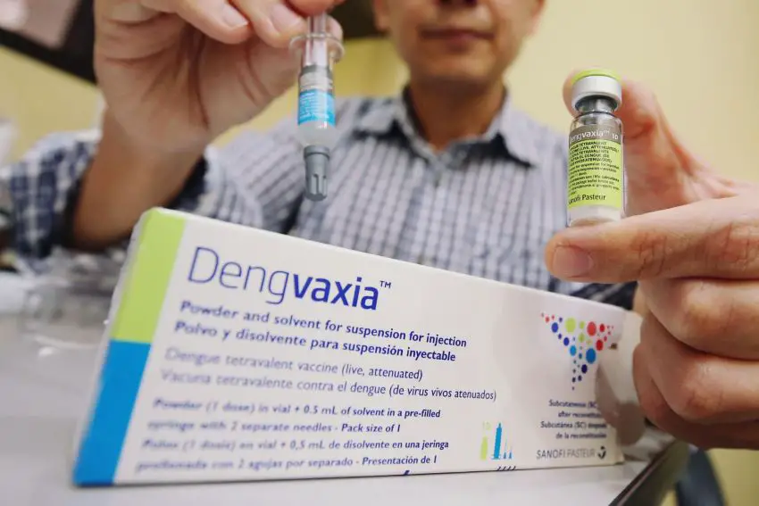 Box of Dengvaxia vaccine, in background person's hands holding vials of the vaccine