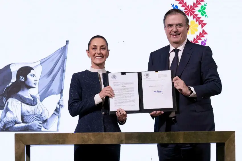 La presidenta de México, Claudia Sheinbaum, y su ministro de economía, Marcelo Ebrard, se encuentran en una conferencia de prensa frente a una mesa larga y delgada. Juntos están manteniendo una cobertura de cartera con el documento que firmaron para expandir una tarifa del 35% en las importaciones textiles.