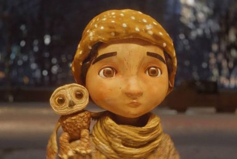 A stop animation still of a little boy in a scarf and and hat with a small owl on his shoulder from the Alfonso Cuaron short film "An Almost Christmas Story"