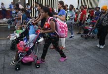 A dark-skinned young woman pushing a child in a stroller leads a group of migrants down a Mexican street, part of a migrant caravan