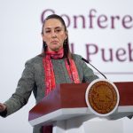 Mexican President Claudia Sheinbaum lead her daily press briefing from a podium, wearing a sweater and scarf