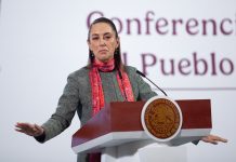 Mexican President Claudia Sheinbaum lead her daily press briefing from a podium, wearing a sweater and scarf