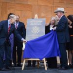 U.S. Ambassador to Mexico Ken Salazar and U.S. Bureau of Overseas Building Operations Director William H. Moser together pull a blue cloth off to reveal a metal plaque bearing the name "Embassy of the United States of America" and the logo of the U.S. Department of State.